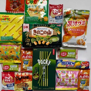 以下が含まれることがあります： カルビーポテトチップス、ポッキーチョコレートスティック、キットカット抹茶バー、フルーツグミなど、日本のスナックの詰め合わせ。さまざまなパッケージの色とデザインが見え、日本語のテキストが表示されています。