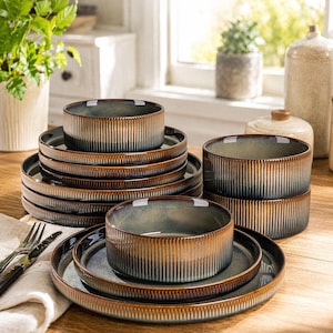 Puede incluir: Un conjunto de vajilla de cerámica, que incluye cuencos y platos, en tonos marrones, azules y crema. Las piezas tienen una textura acanalada y un acabado brillante. El conjunto está dispuesto sobre una superficie de madera, lo que sugiere un comedor o una cocina.