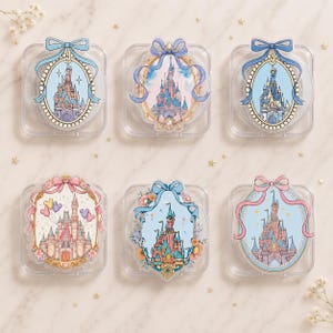 May include: Six square clear acrylic cases, each featuring a decorative oval frame with a castle illustration. The designs include blue, pink, and gold accents, ribbons, bows, and floral details. Each case displays a unique fairy tale castle scene.