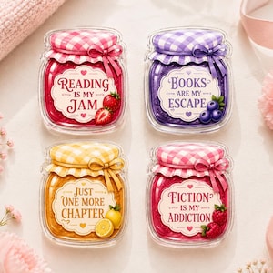 Op de afbeelding: Vier doorzichtige acrylmagneten of pins in de vorm van potjes met ruitjesdeksels en fruitaccenten. De labels bevatten de teksten: Reading is my jam met aardbeien, Books are my escape met bosbessen, Just one more chapter met citroenen en Fiction is my addiction met frambozen.