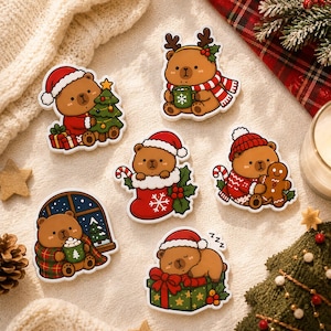 Könnte beinhalten: Ein Set aus sechs gestanzten Aufklebern mit braunen Bären in verschiedenen Weihnachtsszenen. Die Bären tragen Weihnachtsmützen und halten einen geschmückten Baum, eine Tasse, eine Zuckerstange oder einen Lebkuchenmann.