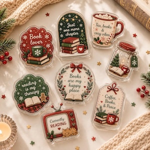 Puede incluir: Una colección de siete adornos de acrílico transparente con ilustraciones festivas y texto. Los diseños incluyen un letrero rojo de book lover, un arco verde con libros, una taza de té, un frasco con un árbol, un letrero verde de lectura y una televisión.