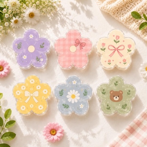 May include: Six flower-shaped containers with clear edges. The top row features a purple floral design, a pink gingham pattern with a bow, and a cream base with tulips and a pink bow. The bottom row shows a yellow floral print with a white bow, a blue daisy pattern, and a green design with a brown bear face.