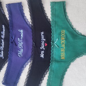 May include: Four ribbed thong panties in black, purple, black, and green, each featuring lace trim, a small center bow, and custom white or gold embroidery. The text reads John Robert McGowan, Mrs. McTavish, Mrs. Janczura with a red heart, and MRS. BLACKWOOD.