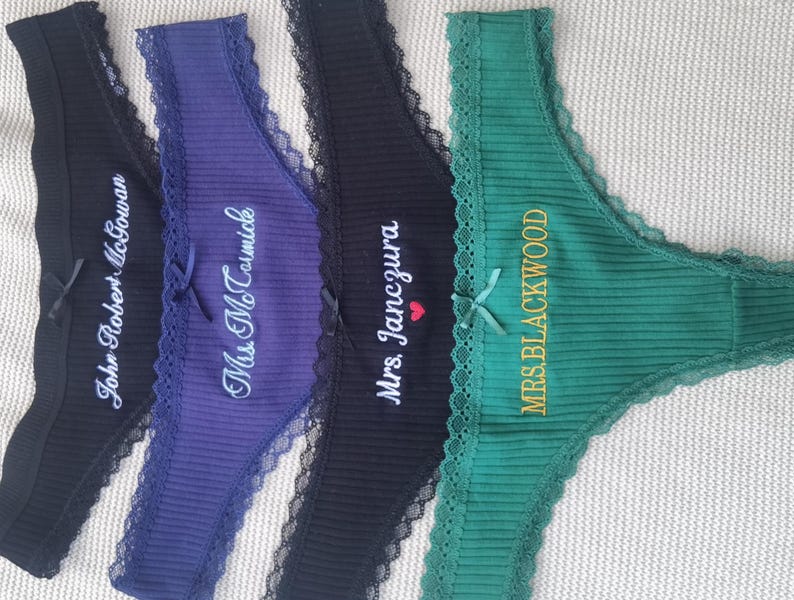 May include: Four ribbed thong panties in black, purple, black, and green, each featuring lace trim, a small center bow, and custom white or gold embroidery. The text reads John Robert McGowan, Mrs. McTavish, Mrs. Janczura with a red heart, and MRS. BLACKWOOD.