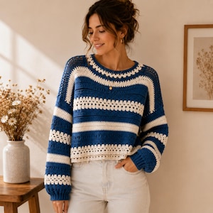 May include: A long-sleeve crochet jumper featuring horizontal stripes in deep blue and cream white. The garment has a round neckline, ribbed cuffs, and a textured pattern created by alternating solid stitches and openwork crochet sections.