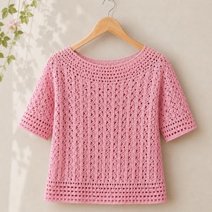 May include: A short-sleeved pink crochet top featuring a wide boat neckline and a repeating vertical openwork pattern. The garment is constructed with a grid-like stitch design throughout the body and sleeves, finished with a horizontal band at the hem.