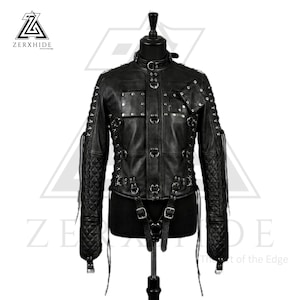 May include: Black leather jacket with multiple metal ring and buckle details. The jacket has a stand-up collar, quilted shoulders, and decorative straps. The brand name "ZERXHIDE" is visible in the upper left corner. The jacket is displayed on a mannequin.