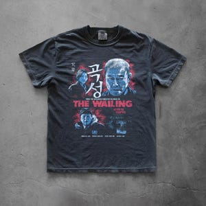 Puede incluir: Una camiseta gris carbón de manga corta con un estampado gráfico de la película The Wailing. El diseño incluye retratos azules y rojos de personajes, texto en coreano, el título The Wailing y la frase Never Be Tempted en color blanco.