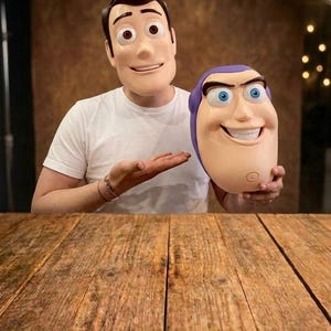 Puede incluir: Una máscara de plástico de Woody con cabello castaño y grandes ojos marrones, y una máscara de plástico de Buzz Lightyear con capucha morada y ojos azules. Ambas máscaras presentan expresiones faciales moldeadas con sonrisas y detalles.