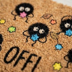 May include: A brown coir doormat with a whimsical design. The mat features black, fluffy creatures with colorful star-shaped accents in pink, blue, and yellow. The word "OFF!" is printed in black at the bottom. Decorative leaves are also included.