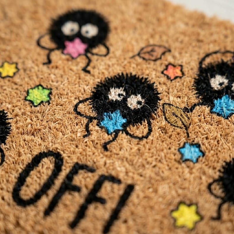 May include: A brown coir doormat with a whimsical design. The mat features black, fluffy creatures with colorful star-shaped accents in pink, blue, and yellow. The word "OFF!" is printed in black at the bottom. Decorative leaves are also included.