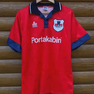 May include: Red vintage soccer jersey with navy blue accents on the collar and sleeves. The jersey features the text "Portakabin" across the front, along with the "York City FC" logo and the "Admiral" logo.