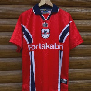 May include: Red York City FC soccer jersey with white and navy blue accents. The jersey features the Portakabin logo across the chest and the York City FC crest. The collar and sleeves have navy blue trim.