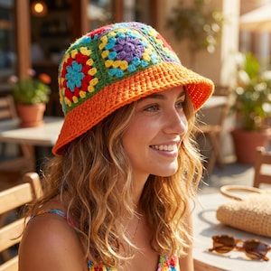 Può includere: Un cappello a secchiello all'uncinetto colorato. Il cappello presenta un design patchwork con quadrati rossi, blu, gialli, verdi e viola. L'orlo è di colore arancione pieno. Il cappello è indossato all'aperto.