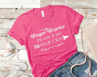 May include: Pink t-shirt with white text that reads "Prayer Warrior Prayer is my War Cry" with an arrow and hearts.