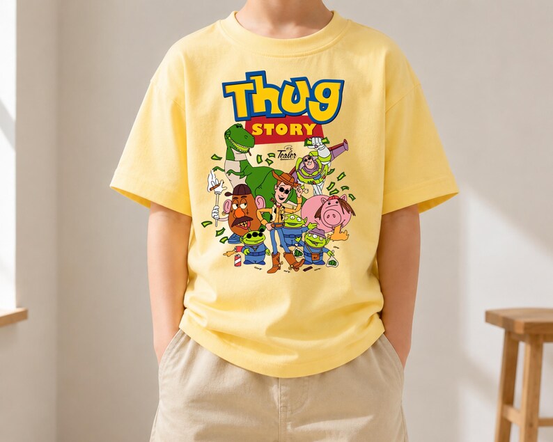 May include: A light yellow short-sleeved t-shirt featuring a graphic print with the text "Thug Story" in blue and yellow letters. The design includes various cartoon characters, including a green dinosaur, a cowboy, and aliens, surrounded by green money.