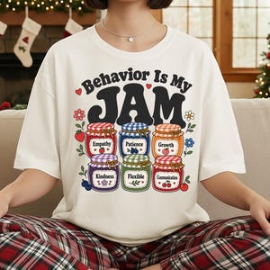 Pode incluir: Uma t-shirt de cor creme com o texto "Behavior Is My JAM" em preto, acompanhada por seis ilustrações coloridas de frascos de compota rotulados com as palavras Empathy, Patience, Growth, Kindness, Flexible e Communication.