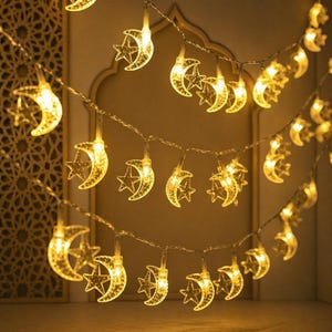 Könnte beinhalten: Dekorative Lichterkette mit leuchtenden Halbmond- und Sternmotiven. Die warmweißen Lichter sind auf einem dünnen Draht aufgereiht und schaffen eine festliche Atmosphäre. Geeignet für Feiertags- oder Eventdekoration. Die Lichter sind warmgelb.