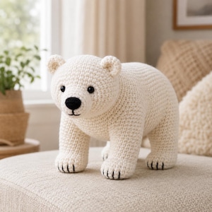 May include: A cream-colored crocheted polar bear toy featuring a textured yarn surface, small rounded ears, black plastic eyes, a black embroidered nose, and black stitched details on the paws, standing in a quadrupedal position.