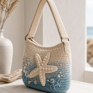 May include: A crochet shoulder bag featuring an ombre colour transition from cream at the top to blue at the bottom. The bag is decorated with a large, textured, cream-coloured starfish appliqué, small pearl-like beads, and coral-like accents.