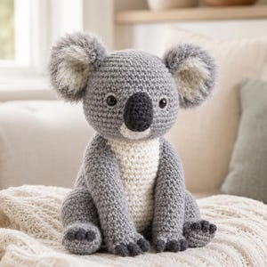 May include: A crocheted koala stuffed animal featuring a gray body, a white chest, and a dark gray nose. The koala has large, fuzzy, round ears with white inner details and dark gray accents on the feet, all crafted with a textured yarn stitch.
