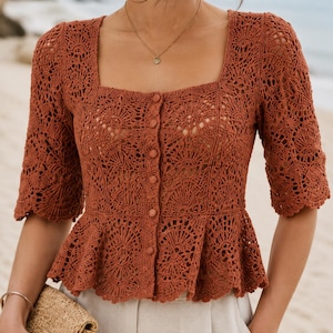 May include: A rust-colored crochet blouse featuring a square neckline, elbow-length sleeves, and a button-down front. The garment is crafted with an intricate openwork floral pattern and includes a flared peplum hem at the waistline.
