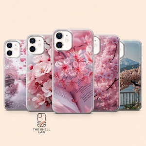 Puede incluir: Cinco fundas transparentes para smartphone con diversos diseños de flores de cerezo. Los patrones incluyen flores de sakura rosas sobre un libro abierto, una escena fluvial con pétalos cayendo y un paisaje montañoso con ramas.