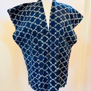 May include: A navy blue kimono-style jacket with a white zigzag pattern. The open-front jacket is displayed on a mannequin. The fabric has a textured appearance. The garment has wide sleeves and a collar that forms a V-neck.