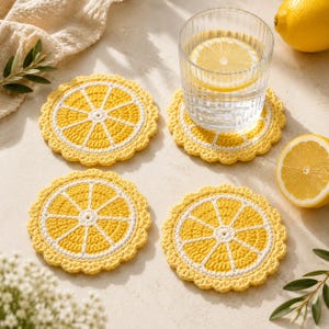 May include: Four handmade crochet coasters in a lemon slice design. The coasters are yellow with white accents and a scalloped edge. A glass of water with a lemon slice sits on one coaster. Lemons and greenery are also in the image.
