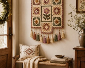 Peut inclure: Une tenture murale artisanale avec un motif floral en patchwork dans des tons crème, vert et bordeaux. Elle est ornée de pompons. Un banc avec un coussin et une couverture à franges est placé en dessous. Ambiance rustique.
