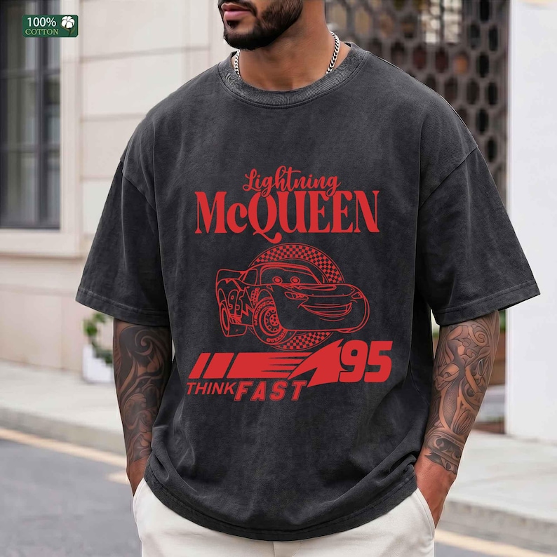 Pu&ograve; includere: T-shirt grigio scuro con grafica rossa di Saetta McQueen del film Cars. Il design include il testo "Lightning McQueen", un'illustrazione di auto, "95" e "Think Fast". La maglietta &egrave; realizzata in 100% cotone.