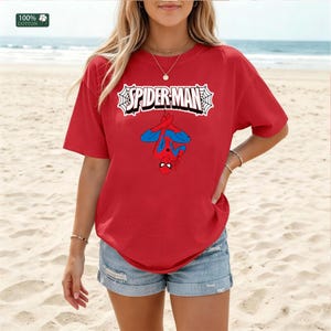 May include: Red t-shirt with the Spider-Man logo and a graphic of Spider-Man hanging upside down. The shirt is made of 100% cotton. The text "SPIDER-MAN" is in a white web-like design.