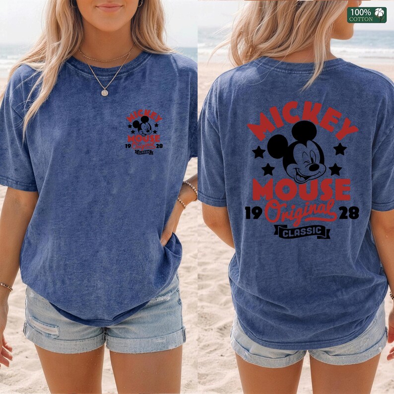 May include: Blue acid wash t-shirt featuring Mickey Mouse graphics. The front displays a small Mickey Mouse design with text, while the back showcases a larger Mickey Mouse graphic with the words "Mickey Mouse Original Classic 1928."