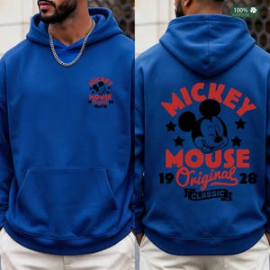 May include: A royal blue hoodie featuring a front and back graphic of Mickey Mouse. The front graphic includes the text "Mickey Mouse 19 Original 28". The back graphic has a larger Mickey Mouse design with the text "Mickey Mouse 19 Original 28 Classic".