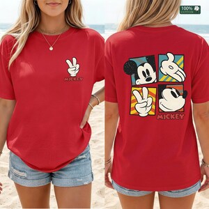 May include: Red t-shirt featuring Mickey Mouse graphics. The front displays a white hand making a peace sign, with "Mickey" below. The back showcases Mickey's face and hands in colorful squares, with "Mickey" at the bottom.