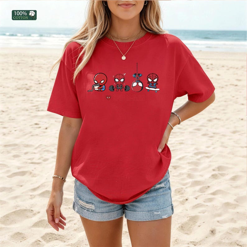 May include: A red short-sleeved t-shirt featuring a graphic print of four small Spider-Man characters performing different activities, including eating noodles, lifting weights, hanging from a web, and skateboarding, with a small heart icon.