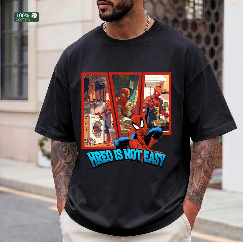 May include: A black short-sleeved t-shirt featuring a graphic print of the character Spider-Man in three separate panels performing household chores, with the text HREO IS NOT EASY printed in large blue letters at the bottom of the graphic.