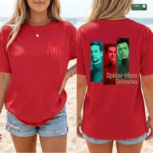 May include: A red short-sleeved t-shirt featuring a small red spider logo on the front chest. The back displays three portraits of men in blue, red, and green frames with the text Spider-Mans Universe. A 100% cotton label is visible in the corner.