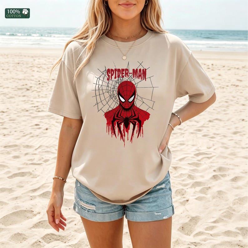 May include: Beige t-shirt featuring a red and black Spider-Man graphic. The graphic includes the text "SPIDER-MAN" above the character's head, with a spider web design in the background. The shirt is made of 100% cotton.