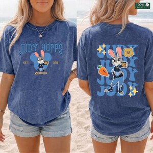 Pu&ograve; includere: Una t-shirt blu con effetto lavaggio acido raffigurante Judy Hopps di Zootropolis. Il davanti mostra il testo Judy Hopps Est. 2016 con un grafico del personaggio. Il retro presenta una grande illustrazione di Judy Hopps, una carota e testo.
