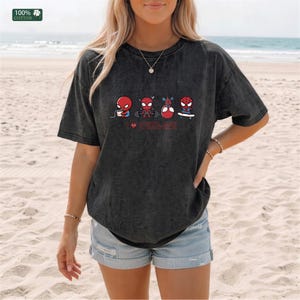 May include: A charcoal gray, acid-wash t-shirt featuring a graphic of four small Spider-Man characters performing different activities, including eating, lifting weights, and skateboarding, with the red text "I ❤️ SPIDER-MAN" printed below.