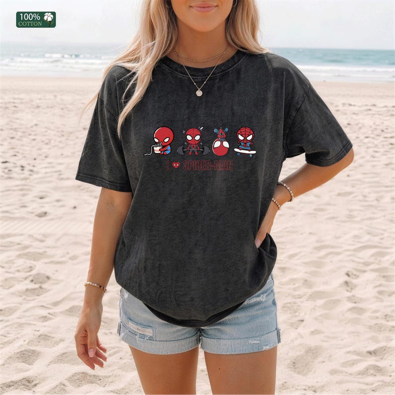 May include: A charcoal gray, acid-wash t-shirt featuring a graphic of four small Spider-Man characters performing different activities, including eating, lifting weights, and skateboarding, with the red text "I ❤️ SPIDER-MAN" printed below.