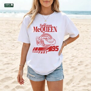 Pu&ograve; includere: T-shirt bianca con grafica rossa di Saetta McQueen del film Cars. Il design include la scritta "Lightning McQueen", un'illustrazione di un'auto e "95 THINK FAST". La maglietta &egrave; in 100% cotone.