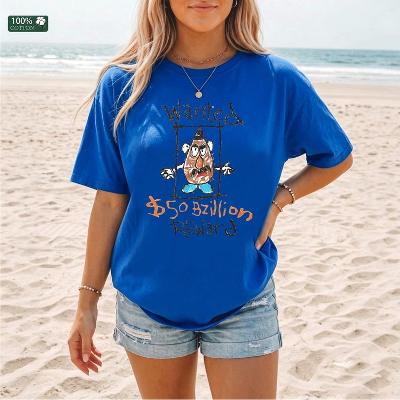 Op de afbeelding: Koning blauw t-shirt met een handgetekende afbeelding van een aardappelachtig personage met de woorden "Wanted" en "$50 Billion Reward". Het shirt is gemaakt van 100% katoen.