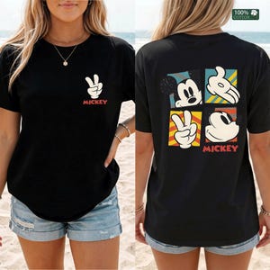 May include: Black t-shirt featuring a Mickey Mouse design. The front displays a peace sign hand gesture and the word "Mickey" in red. The back showcases four Mickey Mouse images in colorful squares, with the word "Mickey" at the bottom.