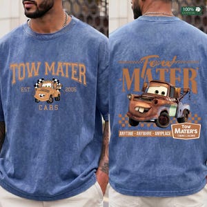 May include: A blue acid-wash t-shirt featuring a graphic of the character Tow Mater. The front displays the text Tow Mater Est. 2006 Cars. The back features a larger illustration of the character with the text Tow Mater Anytime Anywhre Anyplace.