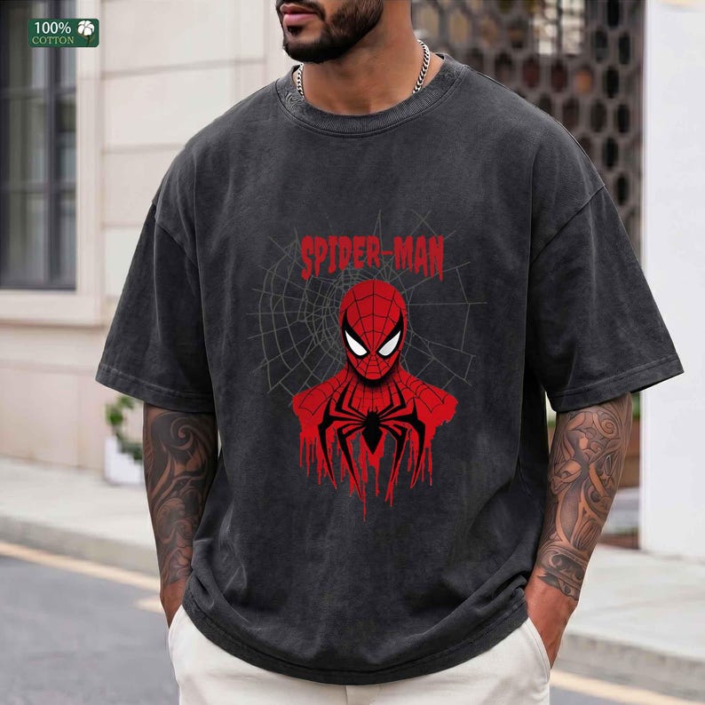 May include: Dark gray t-shirt featuring a red Spider-Man graphic. The design includes the words "Spider-Man" above a stylized image of the superhero with a spiderweb background. The shirt is made of 100% cotton.