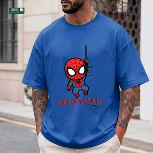 Op de afbeelding: Blauw T-shirt met een cartoon Spider-Man afbeelding. Het ontwerp toont een rood en blauw Spider-Man karakter dat aan een web hangt, met het woord "SPIDERMAN" in rode letters eronder. Het shirt is gemaakt van 100% katoen.