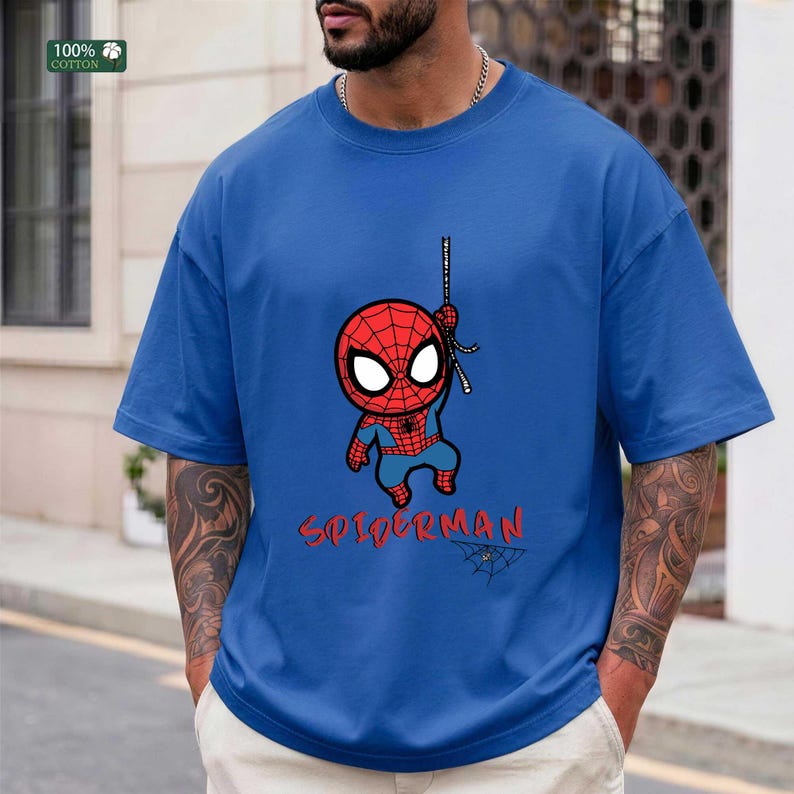 Op de afbeelding: Blauw T-shirt met een cartoon Spider-Man afbeelding. Het ontwerp toont een rood en blauw Spider-Man karakter dat aan een web hangt, met het woord "SPIDERMAN" in rode letters eronder. Het shirt is gemaakt van 100% katoen.